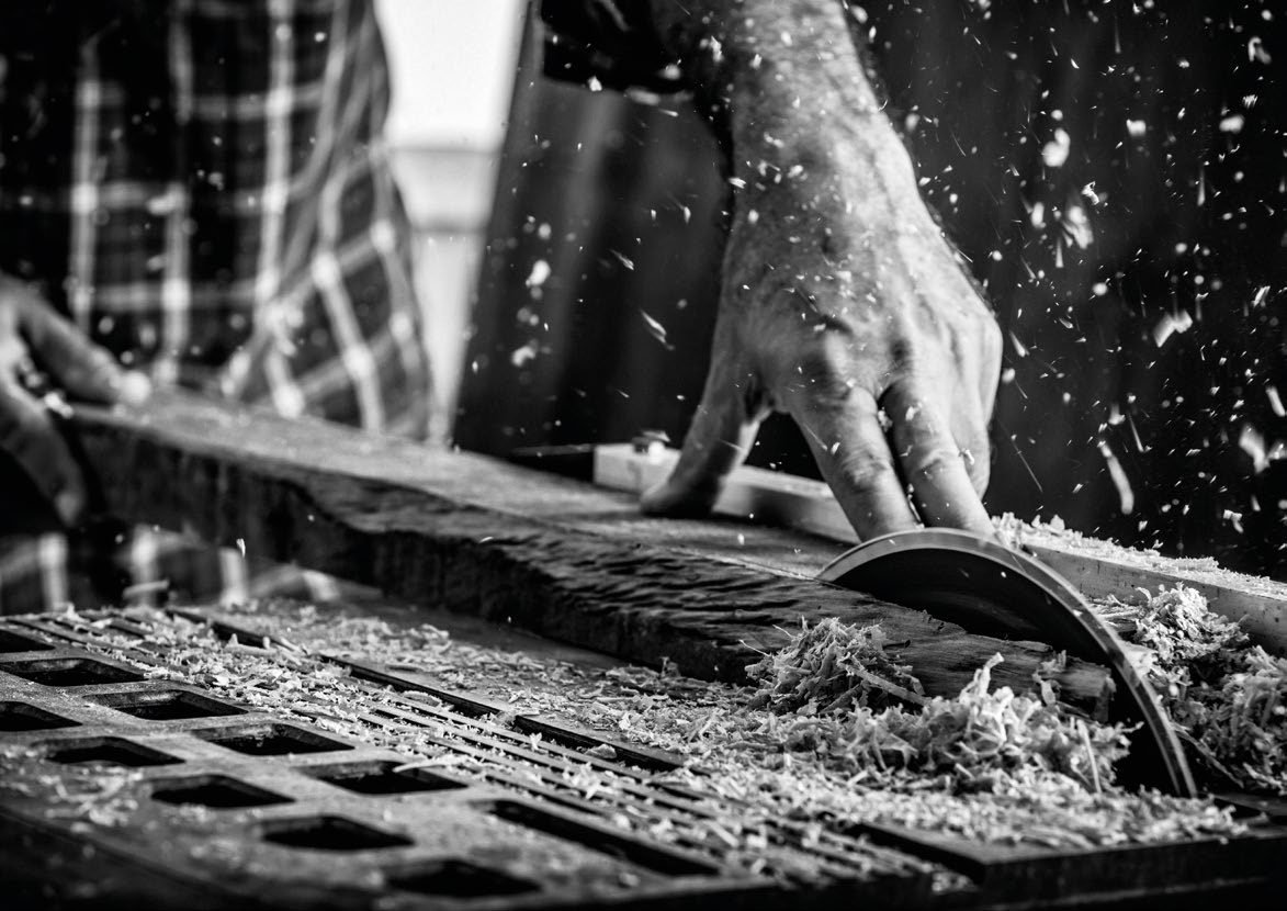 Handwerker beim Hobeln einer Massivholzbohle in der Werkstatt von Acqua Natura
